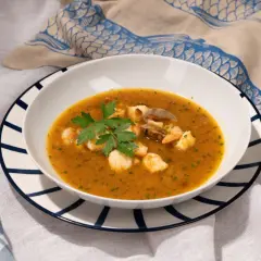 Un plato de sopa de pescado con trozos de marisco, gambas y mejillones, decorado con perejil fresco.