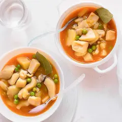 Dos cuencos de sepia con patatas y guisantes en salsa. Un vaso de agua al lado.