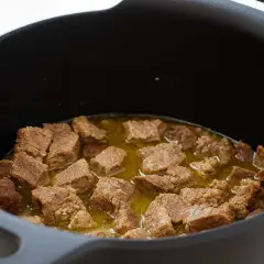 Trozos de magro con tomate cocinándose en una olla negra.
