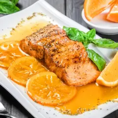 Delicioso salmón a la naranja, servido con rodajas de naranja y hojas de albahaca fresca.