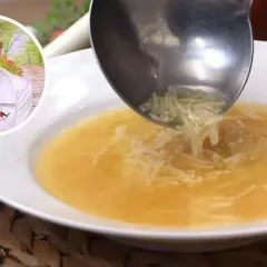 Un chef sirve sopa de fideos en un plato blanco. El caldo dorado y los finos fideos se ven deliciosos.