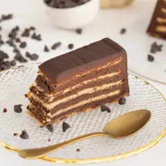 Rebanada de tarta de galletas de la abuela, con capas de galleta y chocolate, decorada con chispas de chocolate y una cuchara dorada.