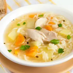 Un reconfortante plato de sopa de pollo con fideos, trozos de zanahoria y patata, adornado con perejil fresco.