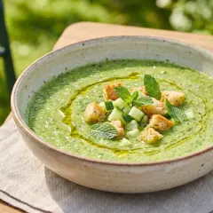 Gazpacho de calabacín refrescante, adornado con cubitos de pepino, picatostes crujientes y hojas de menta.