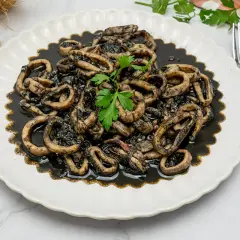 Calamares en su tinta, una receta tradicional servida en un plato blanco con un tenedor y perejil fresco.