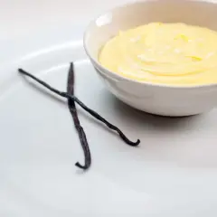 Crema inglesa cremosa en un tazón, con dos vainas de vainilla oscuras al lado.