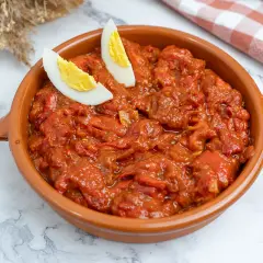 Un sabroso asadillo manchego en cazuela de barro, decorado con gajos de huevo cocido.