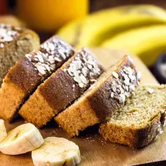 Rebanadas de bizcocho de plátano sin azúcar, cubiertas con avena, junto a plátanos frescos y un tazón de avena.