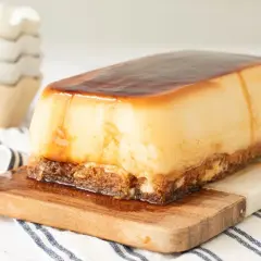 Tarta de cuajada rectangular con caramelo líquido, servida sobre tabla de madera.