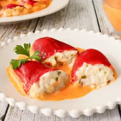 Pimientos del piquillo rellenos de bacalao, cubiertos en una cremosa salsa naranja, adornados con perejil fresco.