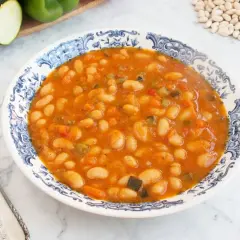 Un plato de alubias blancas con verduras, cocinadas en una salsa sabrosa. Se ven trozos de pimiento, zanahoria y calabacín.