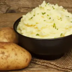 Un cremoso puré de patatas Thermomix, adornado con perejil picado, junto a patatas frescas sobre una mesa de madera.