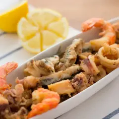 Deliciosa fritura de pescado con gambas y calamares, servida en una bandeja blanca con gajos de limón.