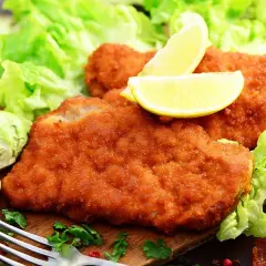 Dos filetes empanados dorados, servidos con lechuga fresca, limones y coles de Bruselas. Un plato delicioso y crujiente.