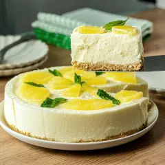 Una porción de tarta de piña sin horno, cremosa y decorada con piña y menta, se levanta de la tarta completa.