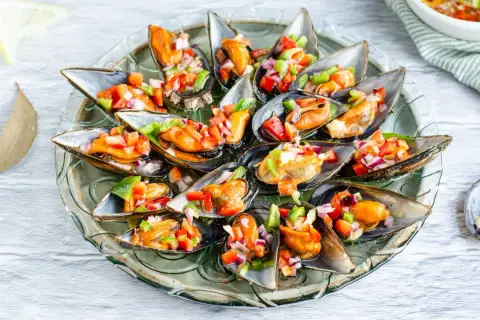 Mejillones a la vinagreta, frescos y coloridos, servidos en una bandeja de cristal.
