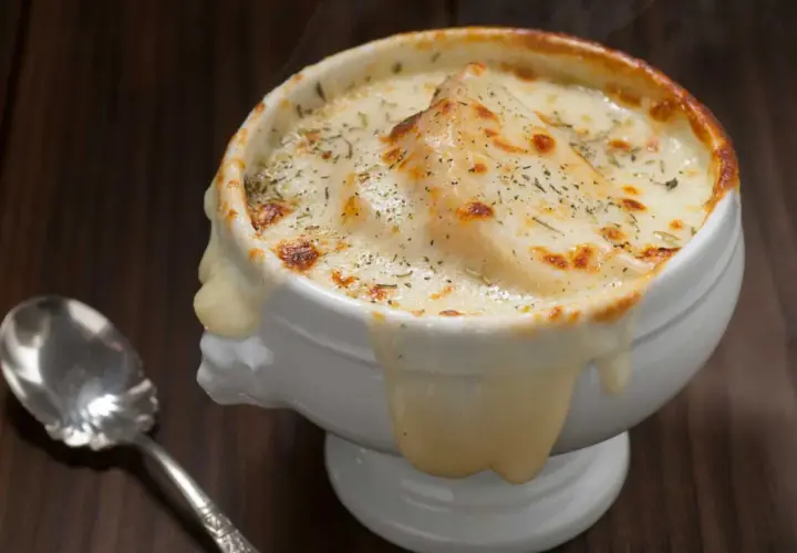 Sopa de cebolla gratinada, con queso derretido y hierbas, humeante y deliciosa, lista para ser disfrutada con una cuchara.