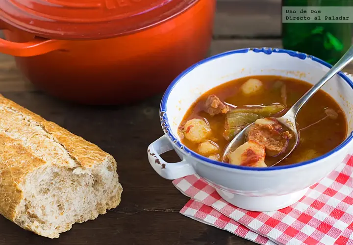 Un plato humeante de patatas a la riojana, con chorizo y pimientos, acompañado de pan rústico y una olla roja.