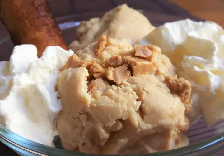 Delicioso helado de turrón con trozos crujientes, acompañado de nata montada y un bizcocho dorado.