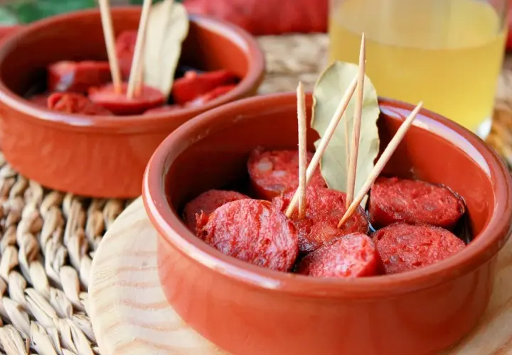 Dos cuencos de barro con chorizos a la sidra, decorados con palillos y hojas de laurel.