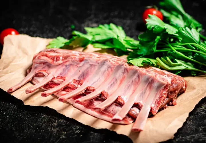 Costillar de cordero crudo, listo para preparar un delicioso cordero al chilindrón con perejil y tomates.