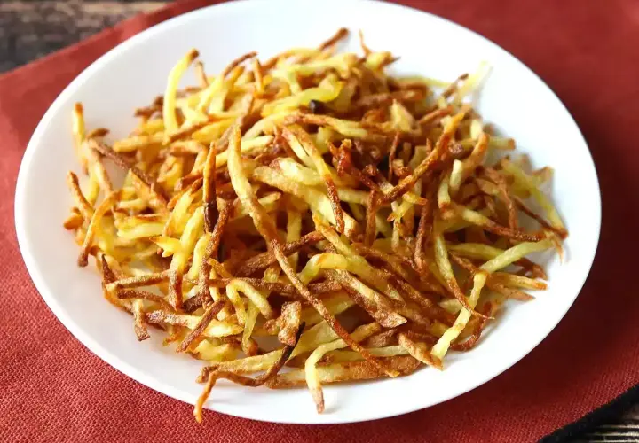 Un plato blanco lleno de crujientes patatas paja doradas, listas para ser disfrutadas.