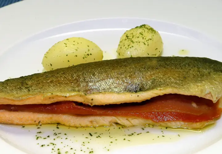 Trucha a la navarra rellena de jamón, servida con patatas cocidas y perejil picado.