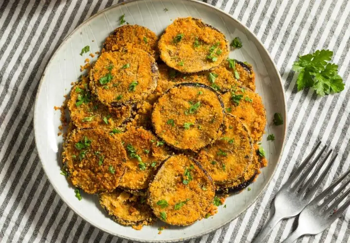 Plato de berenjenas rebozadas, doradas y crujientes, espolvoreadas con perejil fresco.