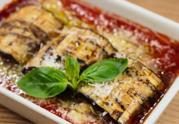 Delicioso pastel de berenjenas gratinado con queso y bañado en salsa de tomate, adornado con hojas de albahaca fresca.