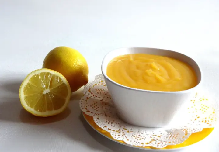 Un tazón de crema de limón, con limones frescos al lado.