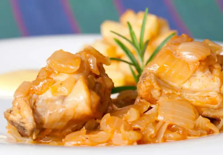 Dos trozos de conejo en escabeche, cubiertos de cebolla caramelizada, acompañados de patatas fritas y una ramita de romero.