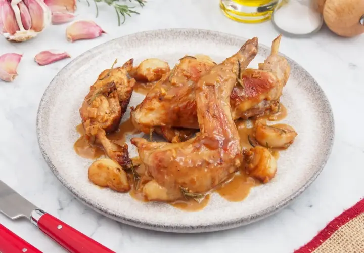 Delicioso conejo al ajillo servido en un plato, con ajos enteros asados y salsa dorada.