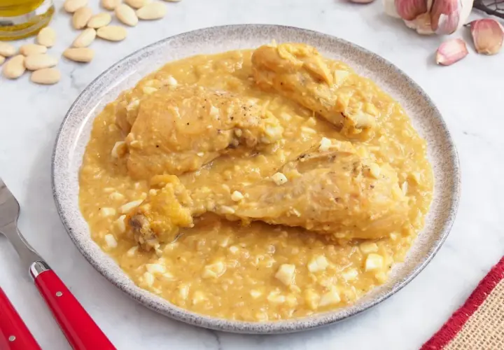 Pollo a la pepitoria servido en un plato, con trozos de huevo duro y almendras esparcidas.