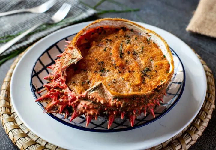 Txangurro a la donostiarra, un delicioso relleno de marisco gratinado en su propio caparazón, adornado con perejil picado.