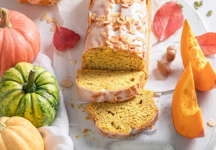 Bizcocho de calabaza, receta de la abuela, con glaseado y almendras. Rodeado de calabazas y hojas de otoño.