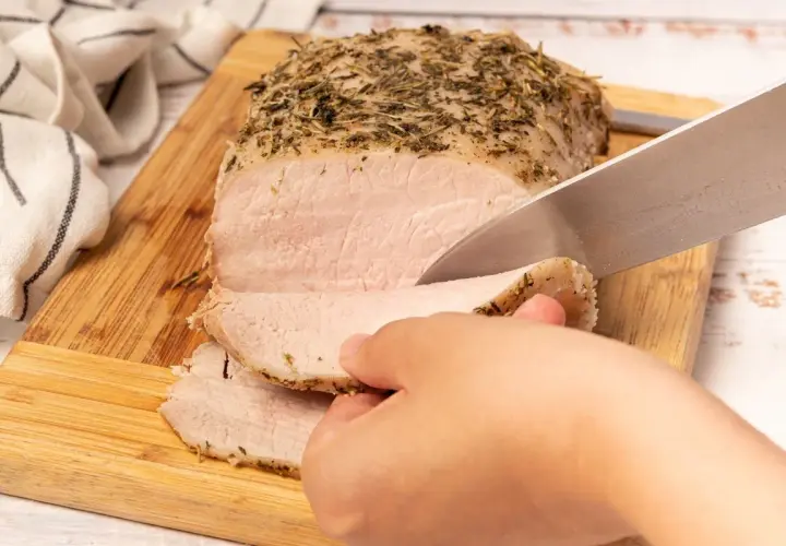 Un jugoso lomo a la sal, recién horneado y cubierto de hierbas, se corta en rodajas tiernas sobre una tabla de madera.