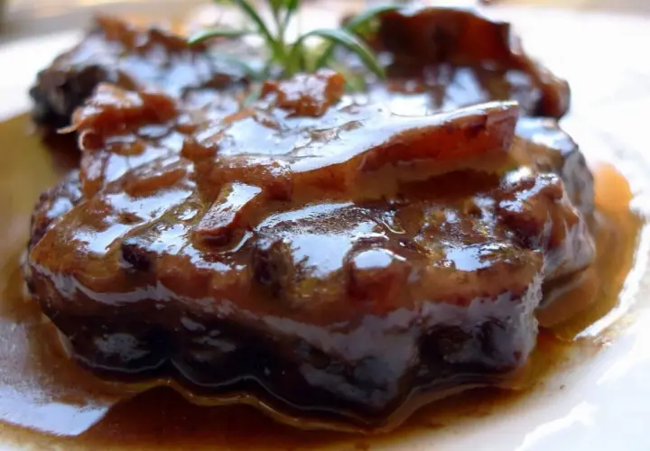 Plato de rabo de toro estofado, con una salsa oscura y brillante, adornado con una ramita de romero.