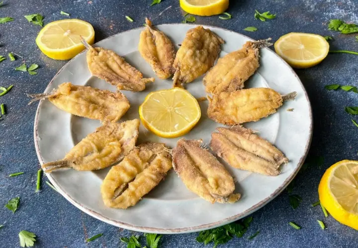 Plato de boquerones fritos crujientes, adornado con rodajas de limón y perejil fresco. Un aperitivo perfecto.