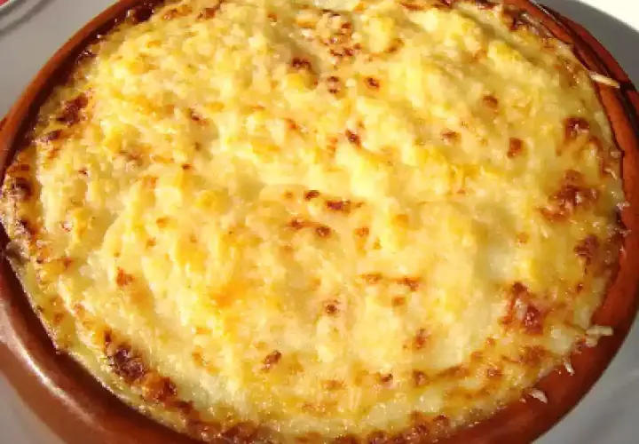 Un delicioso pure de patata gratinado, con bordes dorados y burbujeante, servido en una cazuela de barro.
