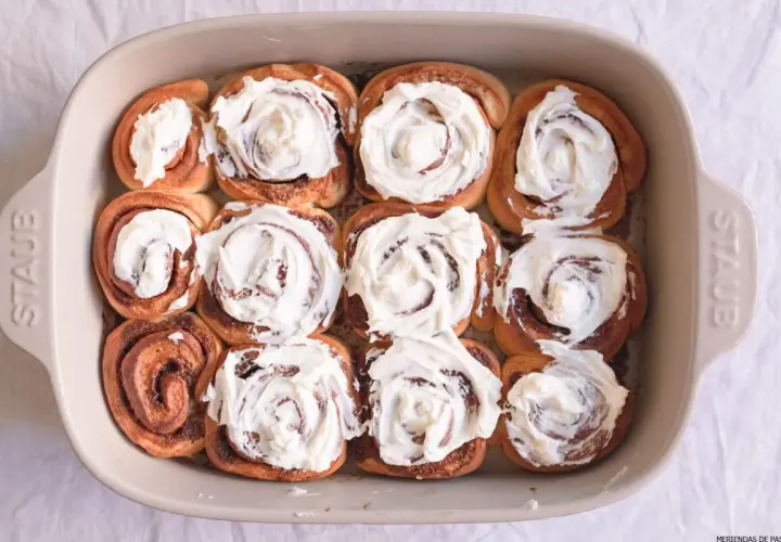 Horneados rollitos de canela cubiertos con glaseado cremoso en un molde de cerámica.