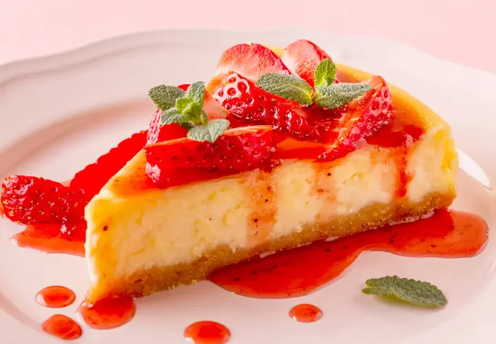 Deliciosa tarta de queso con fresas frescas y salsa de fresa, decorada con hojas de menta.