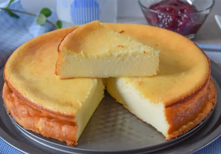 Tarta de queso al horno, dorada y esponjosa, con una porción servida. Un postre casero perfecto.