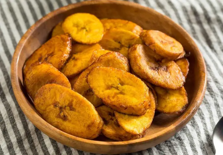 Un tazón de madera lleno de crujientes rodajas de plátano frito, doradas y listas para disfrutar.