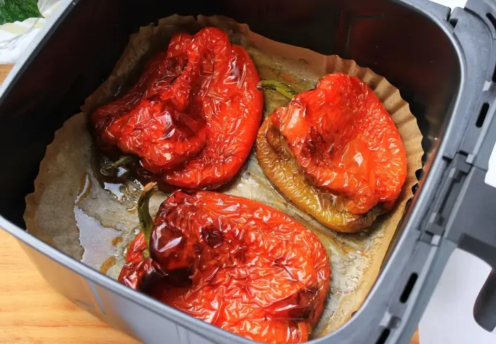 Tres pimientos rojos asados en freidora de aire, con piel arrugada y jugosos, listos para disfrutar.