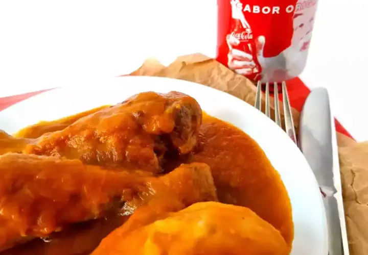 Sabroso pollo a la Coca Cola en un plato blanco, acompañado de cubiertos y una lata de Coca Cola.