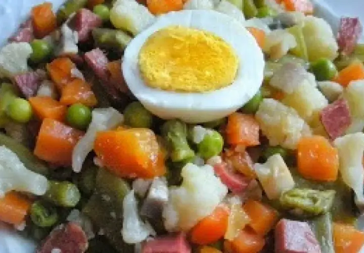 Un plato de menestra de verduras con trozos de zanahoria, guisantes, judías verdes, coliflor y patata, coronado con medio huevo duro.