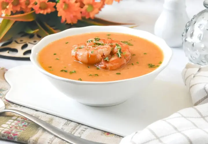 Deliciosa crema de marisco servida en un cuenco blanco, coronada con gambas y perejil picado.