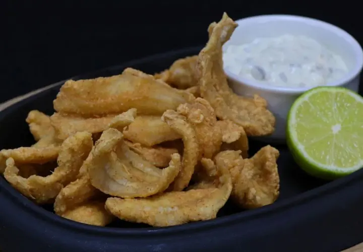 Crujiente bacaladilla frita servida con una salsa cremosa y una rodaja de lima.
