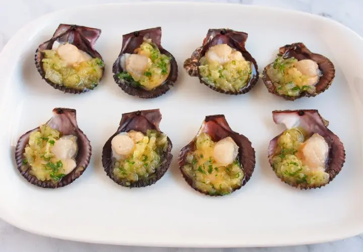 Ocho zamburiñas al horno, listas para disfrutar, con un relleno dorado y perejil picado.