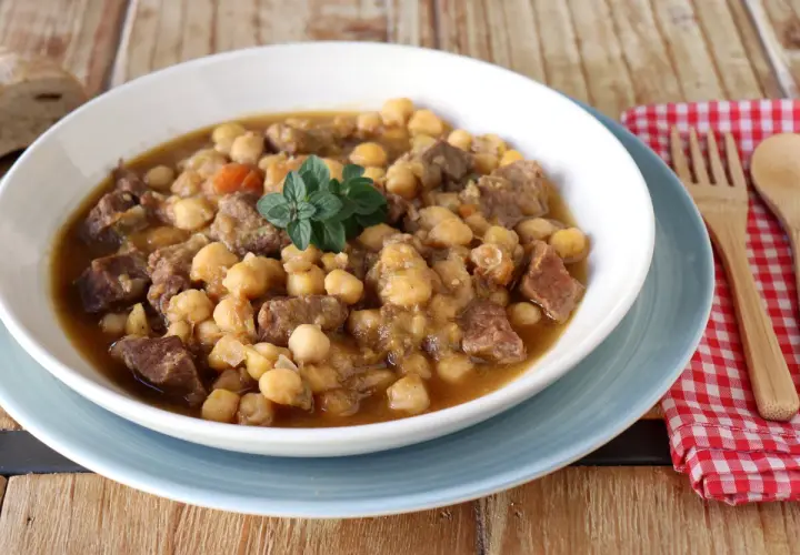 Un plato humeante de garbanzos con carne, perfecto para una receta de garbanzos tradicional. Decorado con una ramita de hierbas frescas.